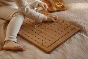 Dziecko bawi się drewnianym geoplanem i uczy się tworzyć figury geometryczne