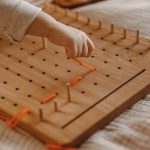 dziecko bawi się drewnianym geoplanem i wyszywa igłą