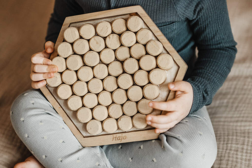 dziecko trzymające drewniany panel sensoryczny z korkiem od wina